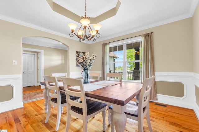 dining room with arched walkways, a tray ceiling, crown molding, light wood finished floors, and a chandelier
