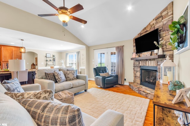 living area featuring vaulted ceiling, a fireplace, ceiling fan, arched walkways, and light wood finished floors