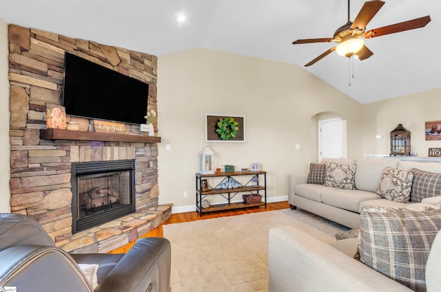 living area featuring vaulted ceiling, a stone fireplace, wood finished floors, ceiling fan, and arched walkways