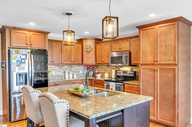 kitchen featuring stainless steel appliances, a sink, a kitchen island with sink, light stone countertops, and hanging light fixtures