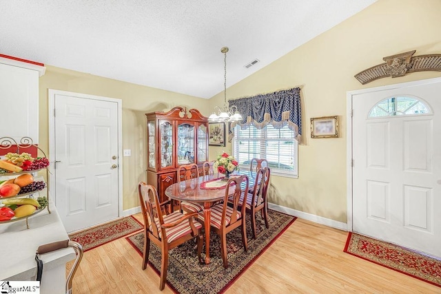 dining room featuring light wood-type flooring, visible vents, lofted ceiling, baseboards, and a notable chandelier