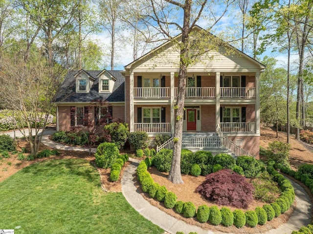 greek revival inspired property with brick siding, a front lawn, covered porch, and a balcony