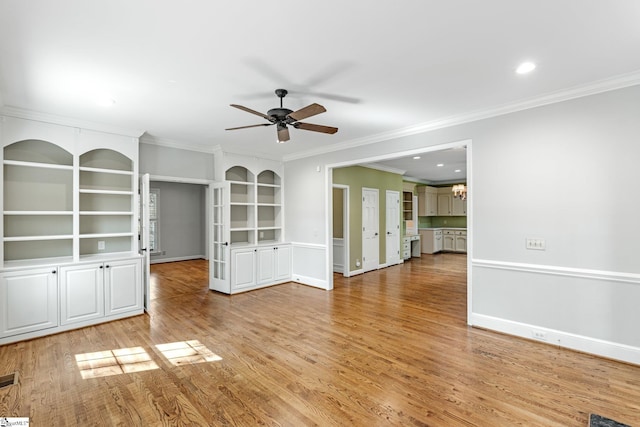 unfurnished living room featuring baseboards, light wood-style floors, ceiling fan with notable chandelier, and crown molding