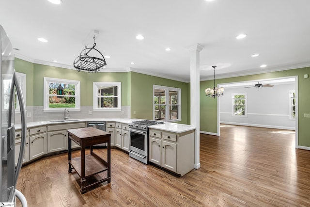 kitchen with a sink, light countertops, appliances with stainless steel finishes, a peninsula, and decorative backsplash