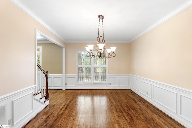 unfurnished dining area with a notable chandelier, ornamental molding, wood finished floors, stairs, and a wainscoted wall