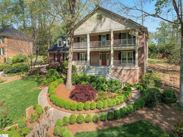 neoclassical / greek revival house featuring a porch, a balcony, a front yard, and brick siding