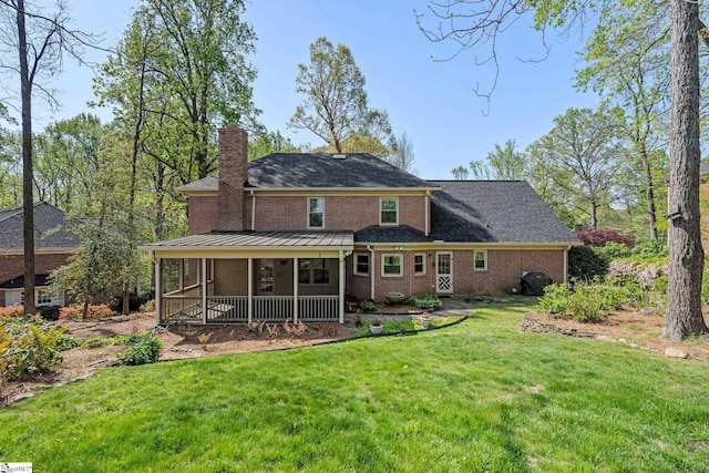 rear view of property featuring a shingled roof, a sunroom, a lawn, a chimney, and brick siding