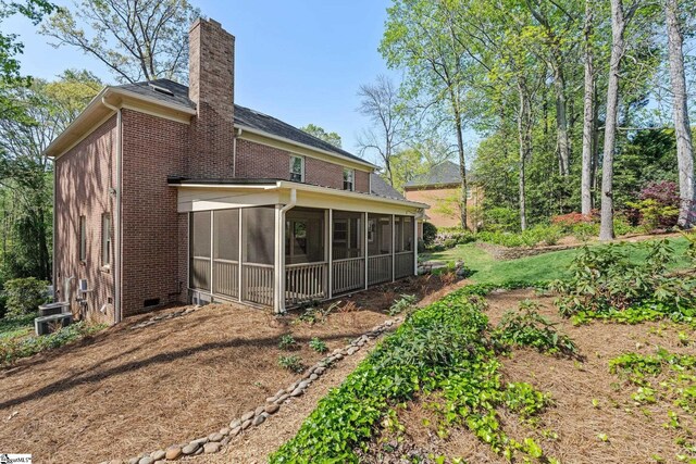 rear view of property featuring a sunroom, a chimney, and brick siding