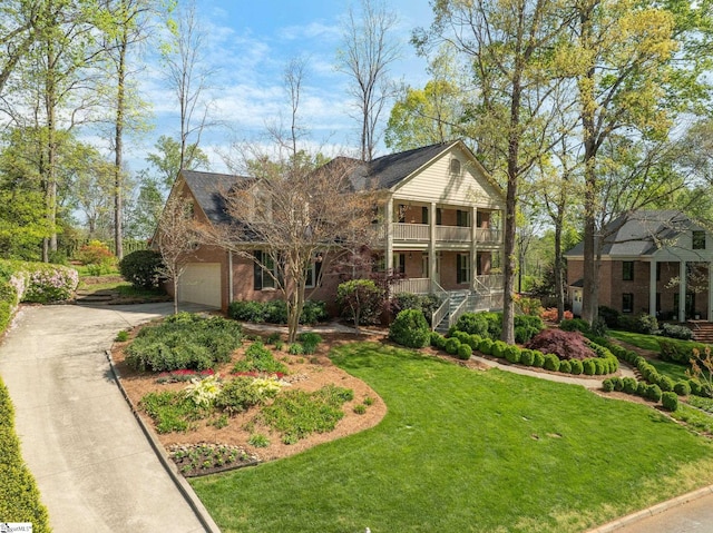 view of front facade with a front yard, covered porch, a balcony, brick siding, and driveway