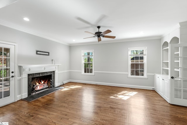 unfurnished living room featuring a warm lit fireplace, ornamental molding, ceiling fan, recessed lighting, and wood finished floors