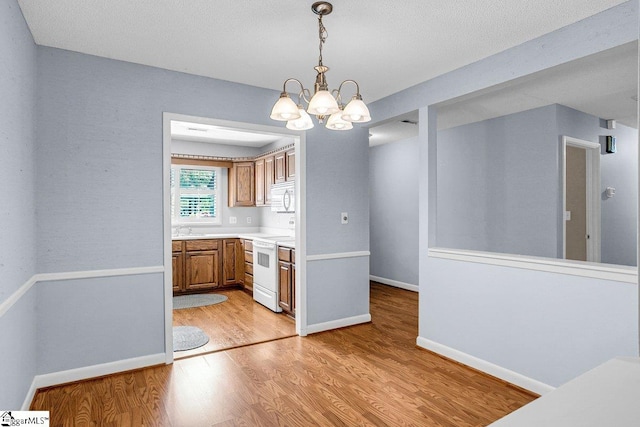 unfurnished dining area featuring a chandelier, a sink, light wood-type flooring, and baseboards