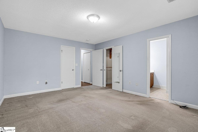 unfurnished bedroom with ensuite bathroom, baseboards, carpet flooring, and a textured ceiling