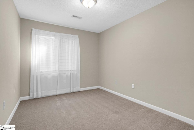 carpeted spare room with visible vents, baseboards, and a textured ceiling