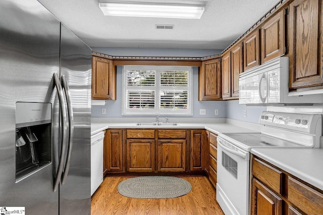 kitchen with white appliances, light wood-style flooring, visible vents, brown cabinets, and a sink