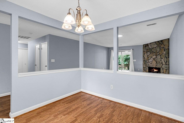 unfurnished dining area featuring wood finished floors, a notable chandelier, a stone fireplace, and visible vents