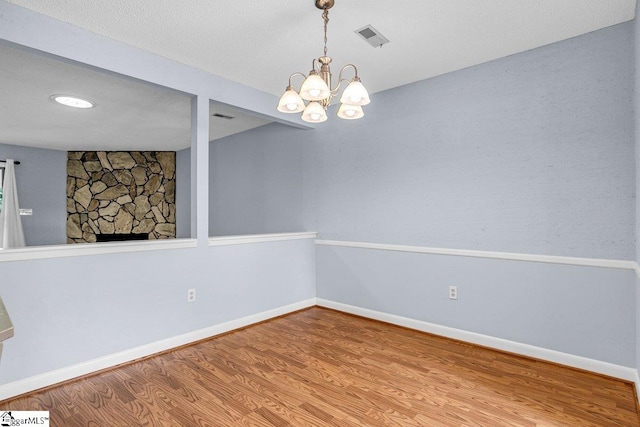 unfurnished room featuring baseboards, an inviting chandelier, a fireplace, visible vents, and wood finished floors