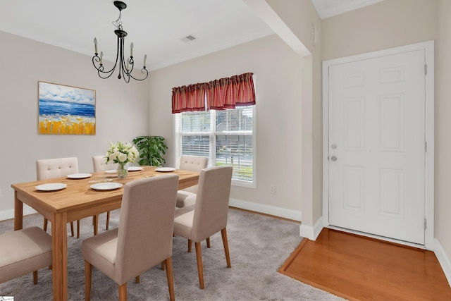 carpeted dining area with visible vents, a notable chandelier, ornamental molding, and baseboards