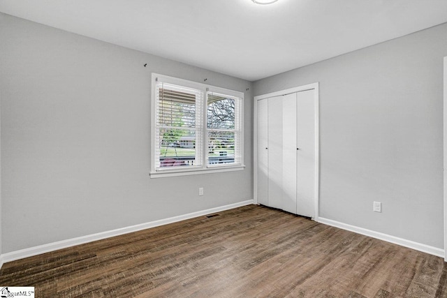 unfurnished bedroom featuring a closet, visible vents, baseboards, and wood finished floors