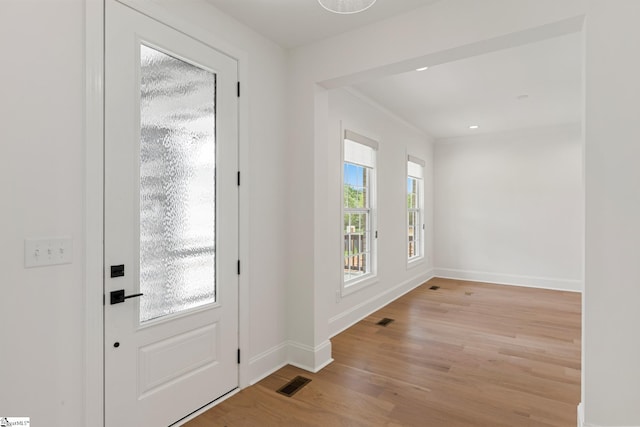 foyer with light wood finished floors, visible vents, baseboards, and crown molding