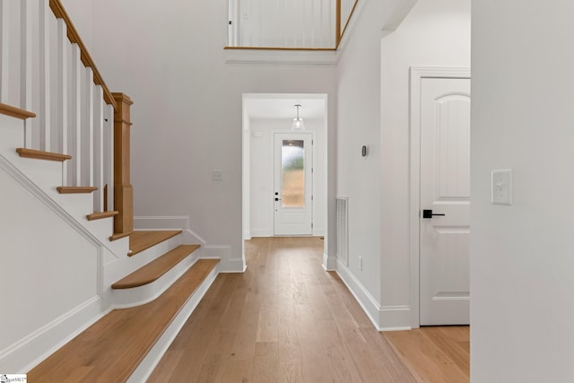 entryway with light wood-style floors, a towering ceiling, visible vents, stairs, and baseboards