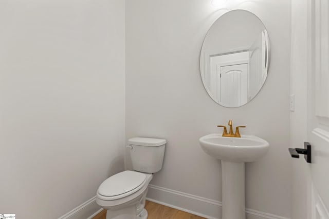 half bathroom with baseboards, a sink, toilet, and wood finished floors