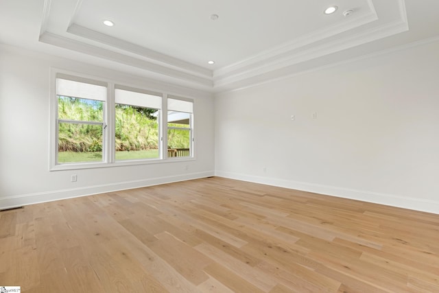 empty room with light wood-style flooring, a tray ceiling, baseboards, and ornamental molding