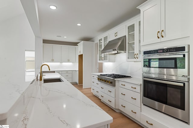 kitchen with white cabinets, a sink, cooktop, under cabinet range hood, and double oven