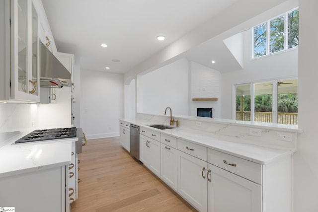 kitchen featuring light wood-type flooring, white cabinets, light stone countertops, dishwasher, and a sink