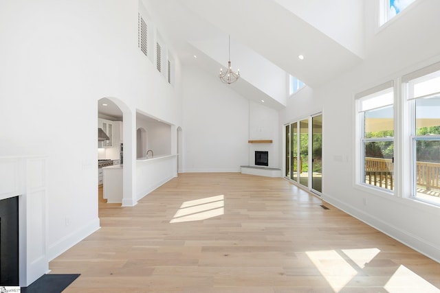 unfurnished living room with a high ceiling, an inviting chandelier, baseboards, and a large fireplace