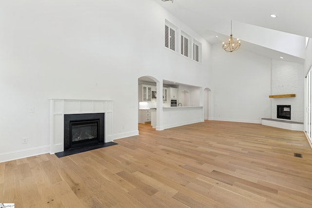 unfurnished living room featuring a notable chandelier, light wood-type flooring, baseboards, a brick fireplace, and high vaulted ceiling