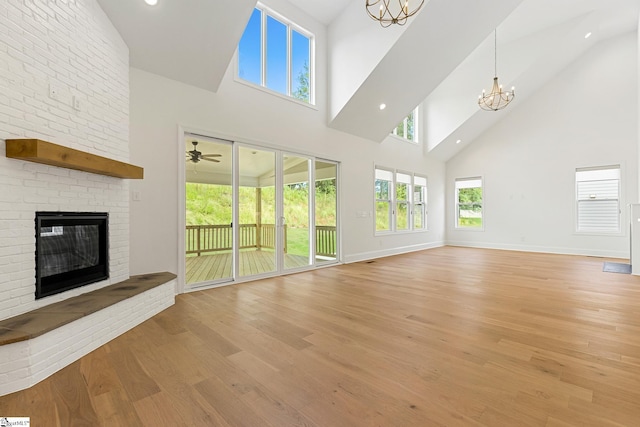 unfurnished living room with high vaulted ceiling, a fireplace, light wood-style flooring, baseboards, and plenty of natural light