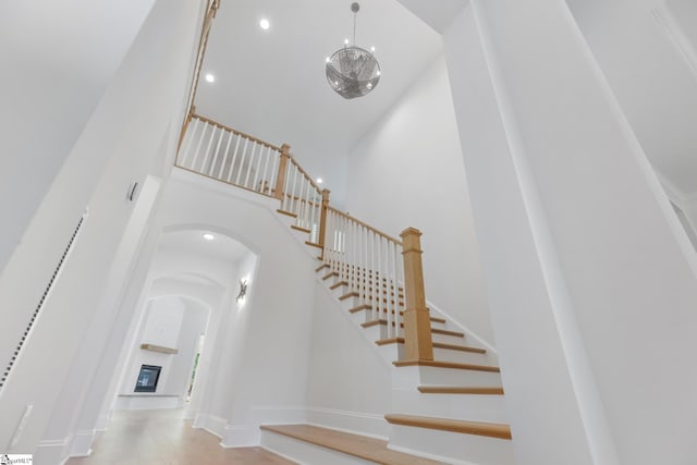 stairway with arched walkways, recessed lighting, a chandelier, a high ceiling, and baseboards