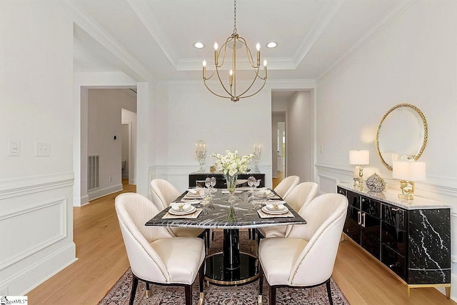 dining space with an inviting chandelier, ornamental molding, light wood-style floors, visible vents, and a raised ceiling
