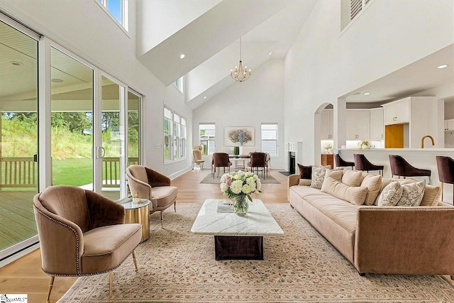 living area featuring visible vents, arched walkways, a notable chandelier, a towering ceiling, and light wood-style flooring