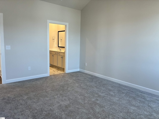 unfurnished bedroom featuring a sink, ensuite bath, light colored carpet, and baseboards