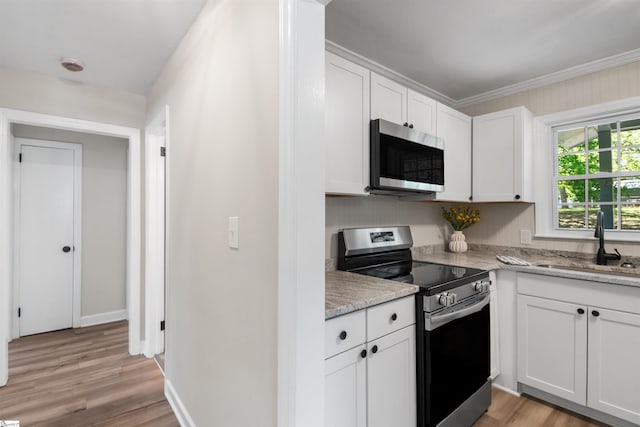 kitchen with a sink, ornamental molding, appliances with stainless steel finishes, white cabinetry, and light wood-style flooring