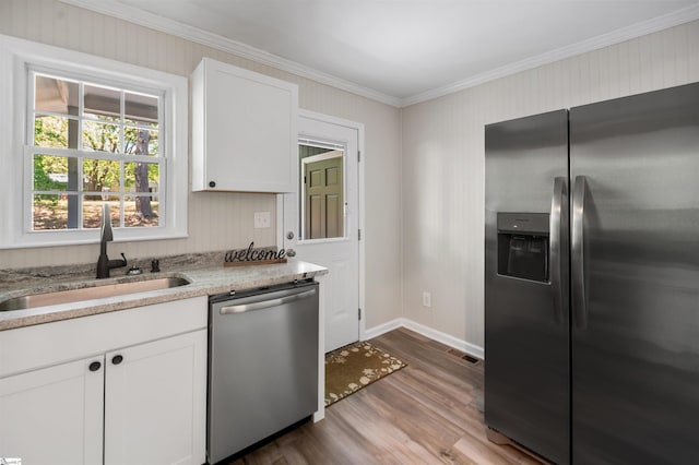 kitchen with ornamental molding, white cabinetry, stainless steel appliances, a sink, and wood finished floors