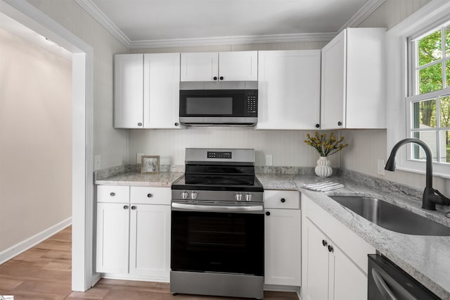 kitchen featuring ornamental molding, white cabinetry, stainless steel appliances, light wood finished floors, and a sink
