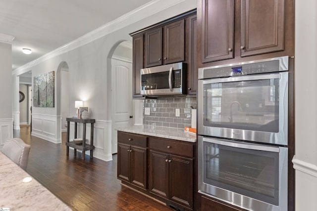kitchen featuring dark wood finished floors, arched walkways, crown molding, dark brown cabinetry, and appliances with stainless steel finishes