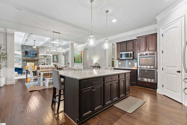 kitchen featuring tasteful backsplash, crown molding, open floor plan, a kitchen bar, and appliances with stainless steel finishes