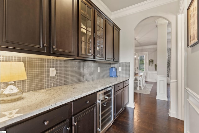 bar with beverage cooler, arched walkways, crown molding, wainscoting, and dark wood-style flooring