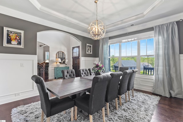 dining room with a wainscoted wall, a tray ceiling, arched walkways, a chandelier, and crown molding
