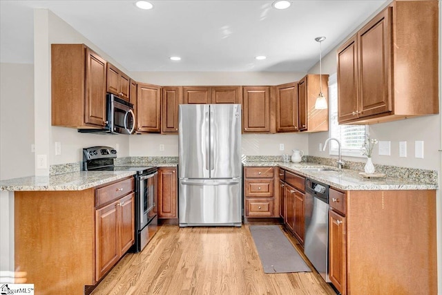kitchen with brown cabinets, light wood finished floors, stainless steel appliances, and a sink