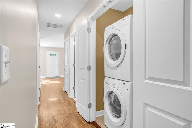washroom featuring light wood finished floors, visible vents, baseboards, stacked washer and dryer, and laundry area