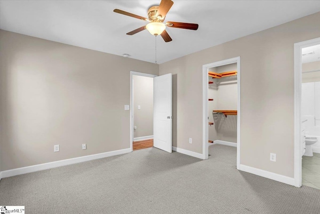unfurnished bedroom featuring baseboards, carpet, a closet, ensuite bath, and a walk in closet
