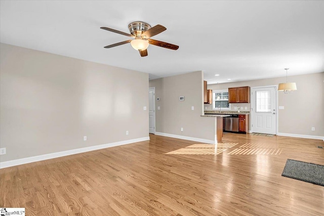 unfurnished living room with light wood-style flooring, baseboards, ceiling fan, and a sink