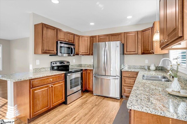 kitchen featuring a sink, light wood-style flooring, a peninsula, brown cabinetry, and appliances with stainless steel finishes