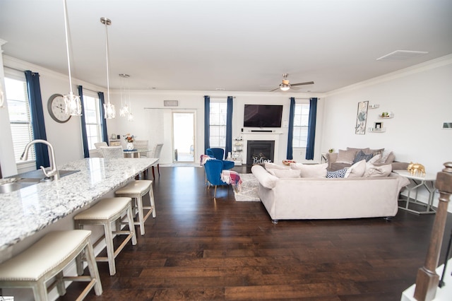 living room featuring ceiling fan, dark wood-style flooring, crown molding, and a fireplace