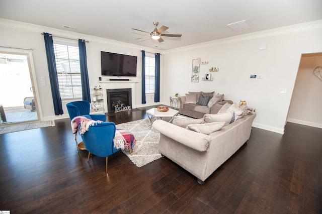 living room with a ceiling fan, crown molding, baseboards, a glass covered fireplace, and dark wood-style flooring