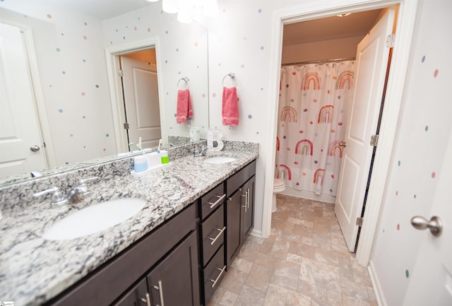 bathroom with stone finish floor, double vanity, toilet, and a sink